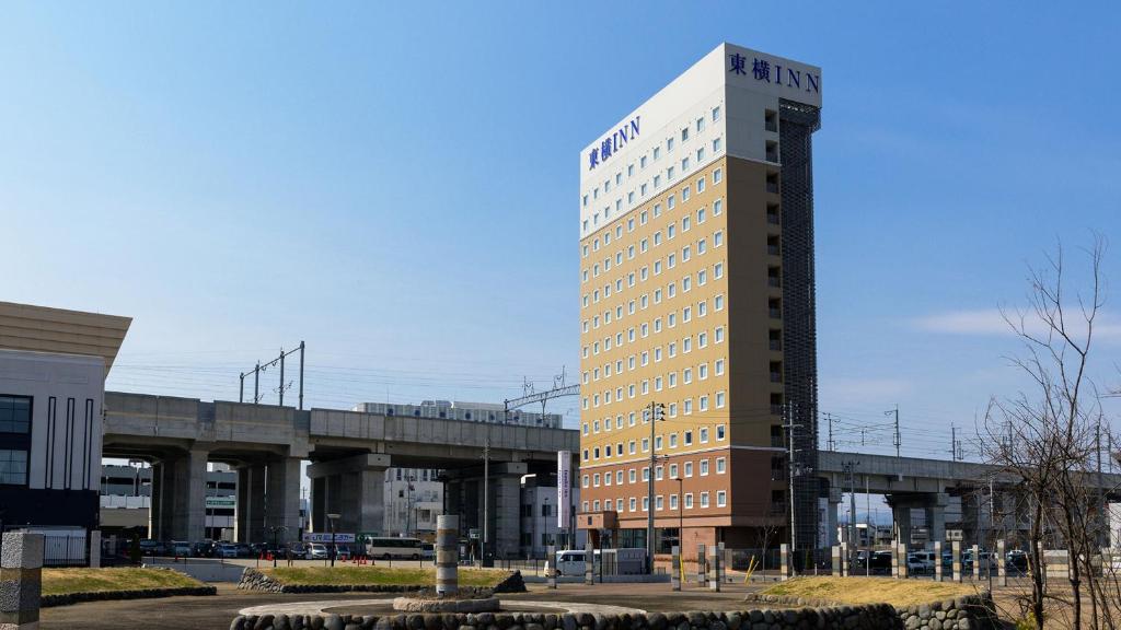 青森Toyoko Inn Shin-Aomori-eki Higashi-guchi的一座高大的建筑,有一座桥在后面