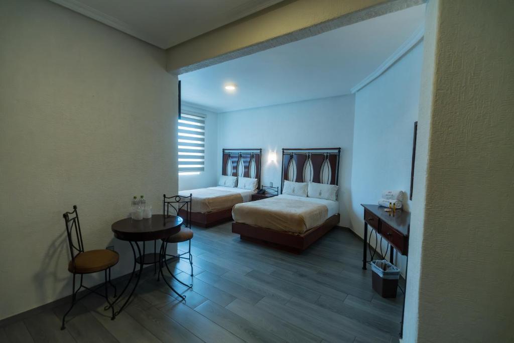 瓜达拉哈拉Hotel Alcazar - Guadalajara Centro Historico的一间卧室配有两张床和一张桌子及椅子