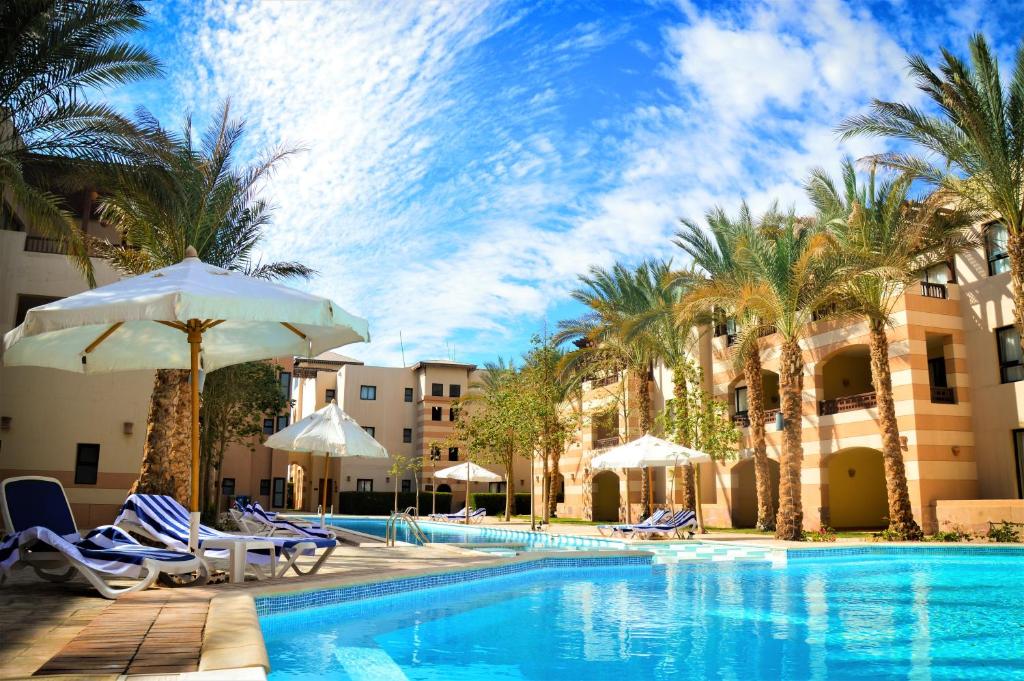加利布港Port Ghalib Marina Residence Suites的一个带椅子和遮阳伞的游泳池以及棕榈树