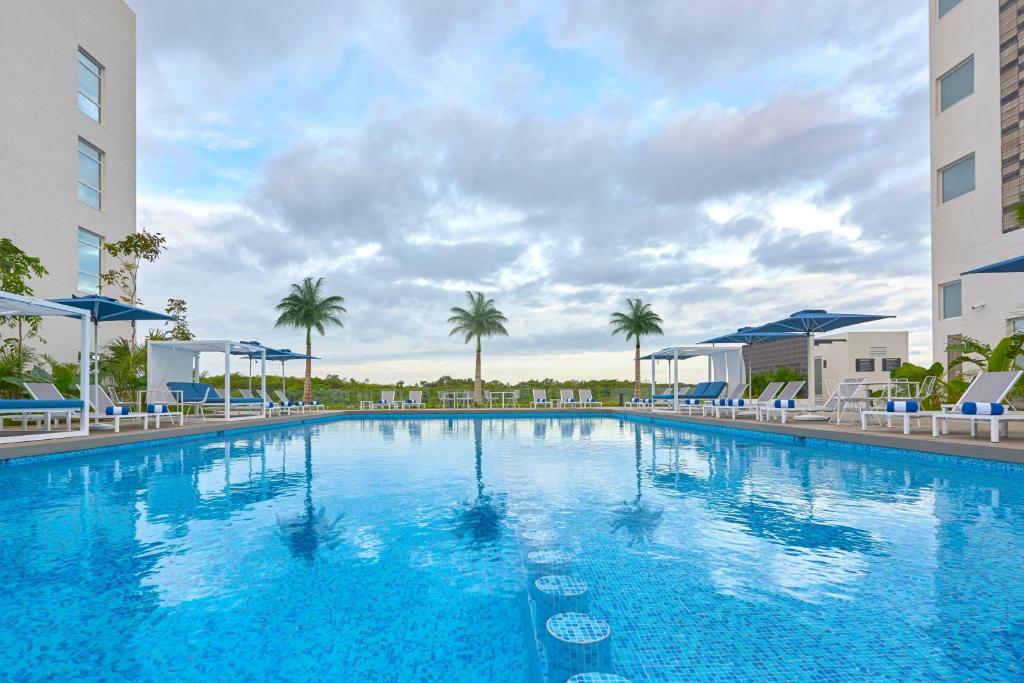 坎昆City Express Plus by Marriott Cancun Aeropuerto Riviera的一个带蓝色椅子和棕榈树的大型游泳池