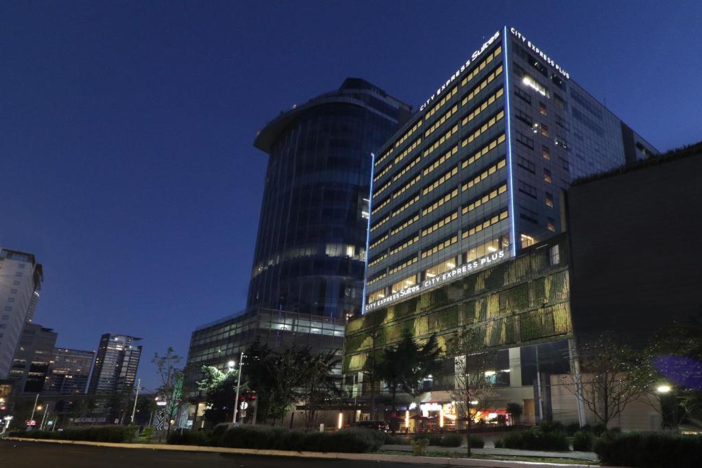 墨西哥城City Express Suites by Marriott Santa Fe的一座高大的建筑,晚上在城市里亮着灯