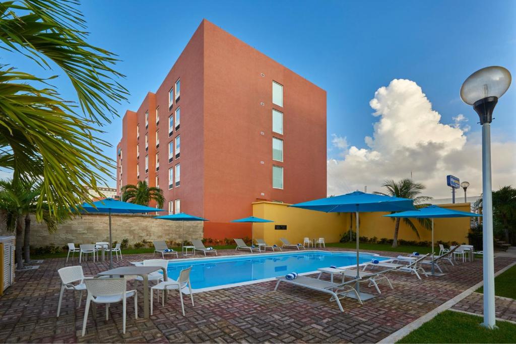 坎昆City Express Junior by Marriott Cancun的一个带游泳池、椅子和遮阳伞的酒店
