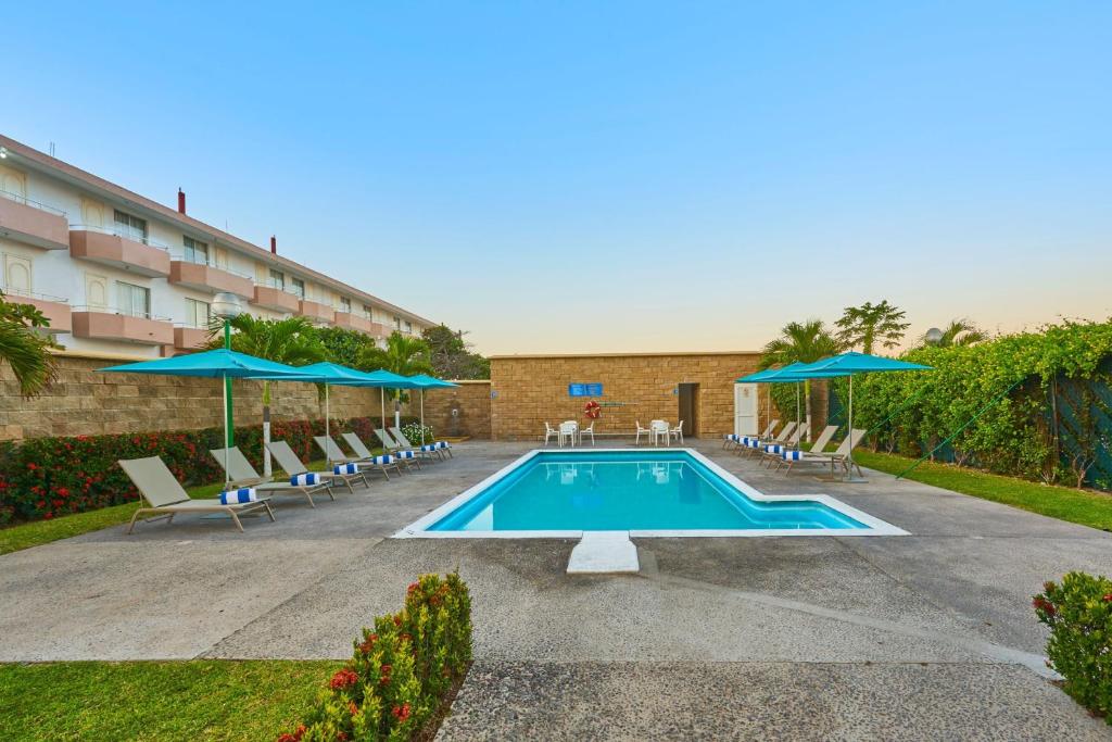 曼萨尼约都市快报曼萨尼约酒店的一座带椅子和遮阳伞的游泳池位于一座建筑旁边