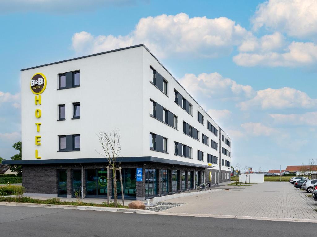 沃尔夫斯堡B&B Hotel Wolfsburg-Weyhausen的一座大型白色建筑,设有停车场