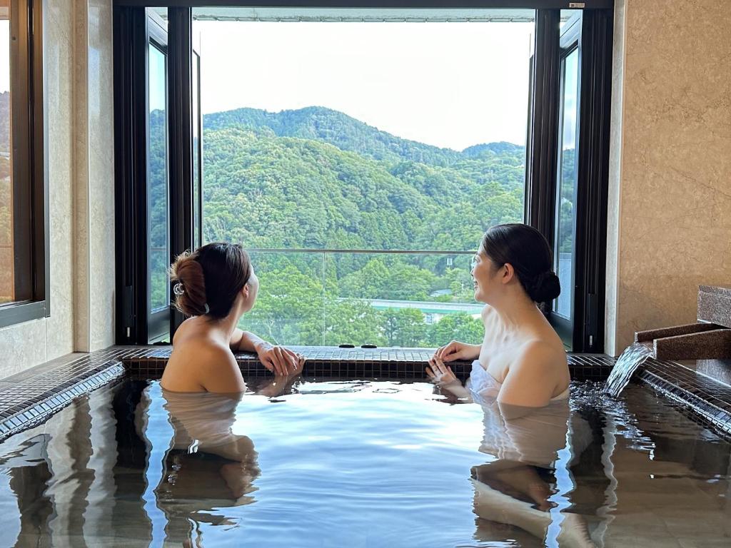 伊东加兰考特宇佐美私人温泉公寓式酒店的两个女人坐在按摩浴缸里,享有美景