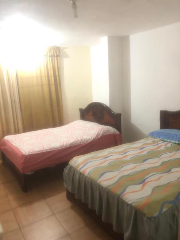 洛哈Pensión Malacatos的一间卧室设有两张床,窗户配有窗帘