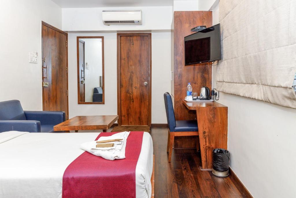 孟买J Hotel and Banquets的酒店客房设有一张床、一张书桌和一台电视机。