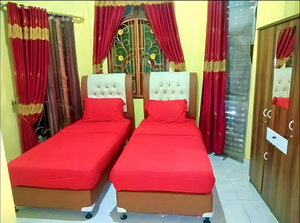 RambahHotel Garuda的配有红色窗帘的客房内的两张床