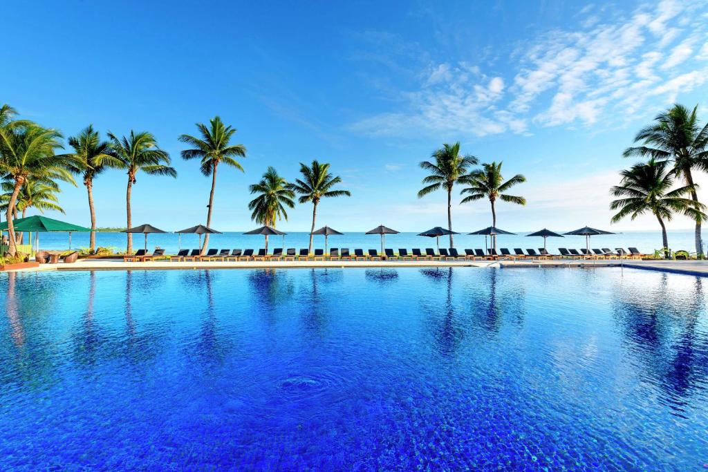 丹娜努斐济海滩希尔顿度假酒店的一座棕榈树和遮阳伞的度假游泳池