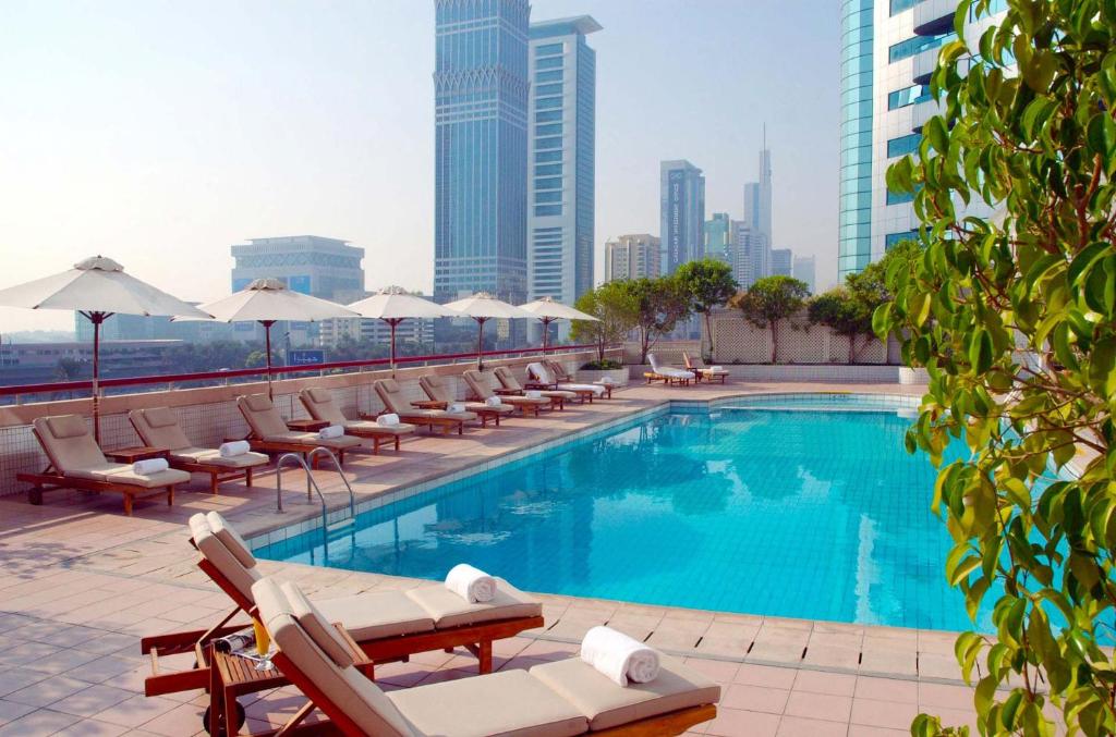 迪拜Millennium Plaza Downtown Suites的一座大楼内的游泳池,配有椅子和遮阳伞