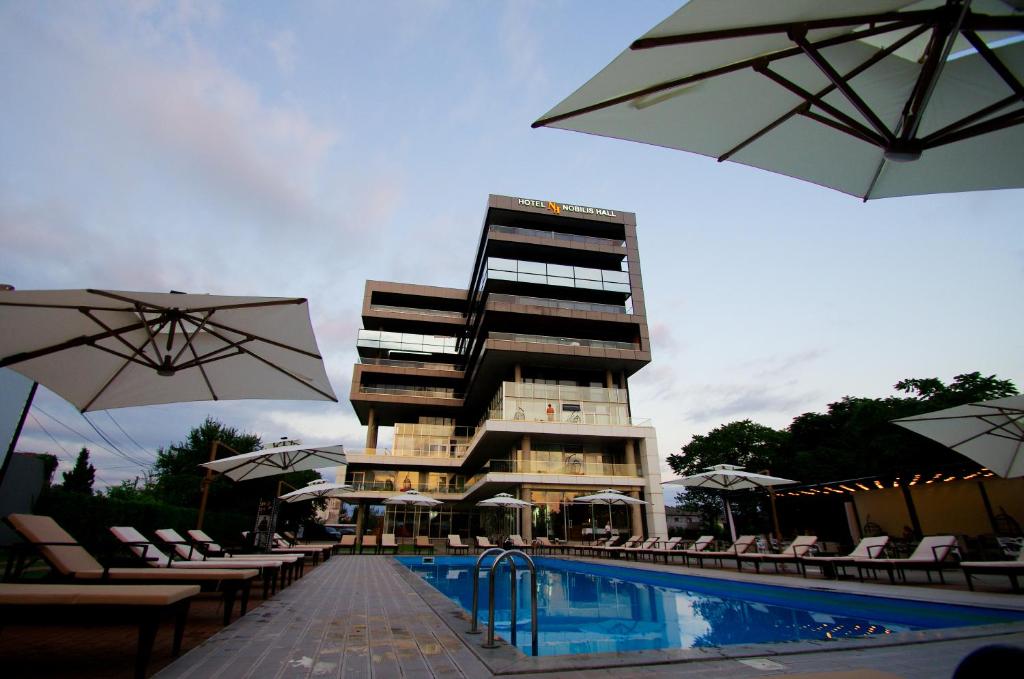 科布列季Hotel Nobilis Hall的一座带游泳池的酒店和一座带遮阳伞的建筑