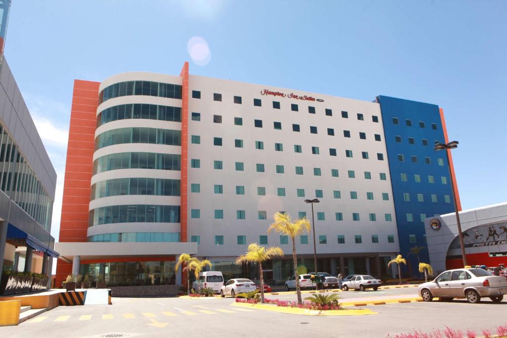 阿瓜斯卡连特斯Hampton Inn & Suites by Hilton Aguascalientes Aeropuerto的停车场内停放汽车的大型建筑