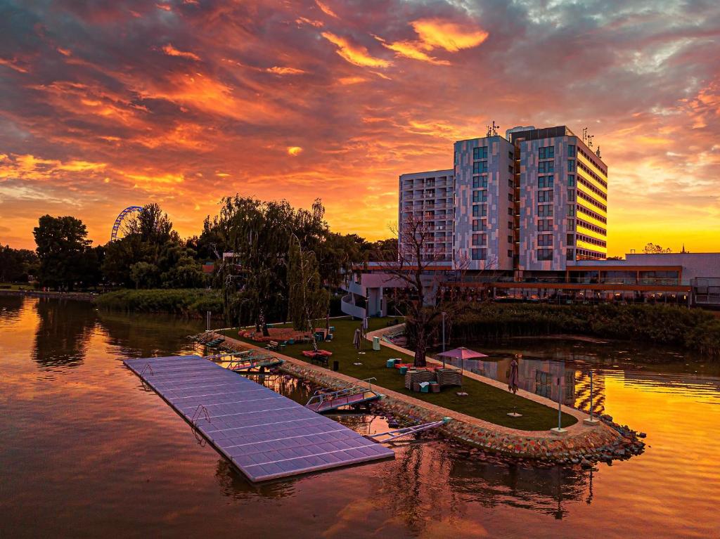 凯斯特海伊Hotel Helikon, Keszthely的一座建筑,在日落时分在水面上设有太阳能电池板