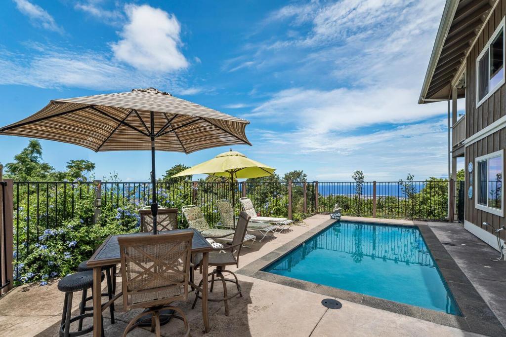 科纳Hale Lio Kai的一个带桌子和遮阳伞的庭院和一个游泳池
