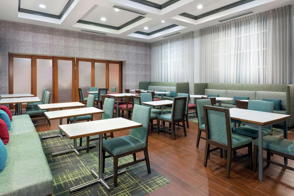 奥兰多汉普顿酒店 - 奥兰多机场村庄通道的有桌椅和窗户的餐厅