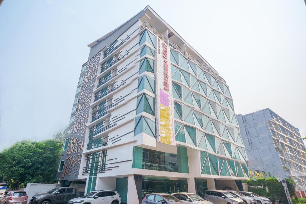 清迈Nimman Mai Design Hotel Chiang Mai - SHA Plus的一座高大的建筑,前面有汽车停放