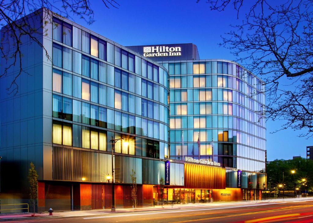 布鲁克林Hilton Garden Inn Boston Brookline, Ma的前面有一条街道的高大的玻璃建筑
