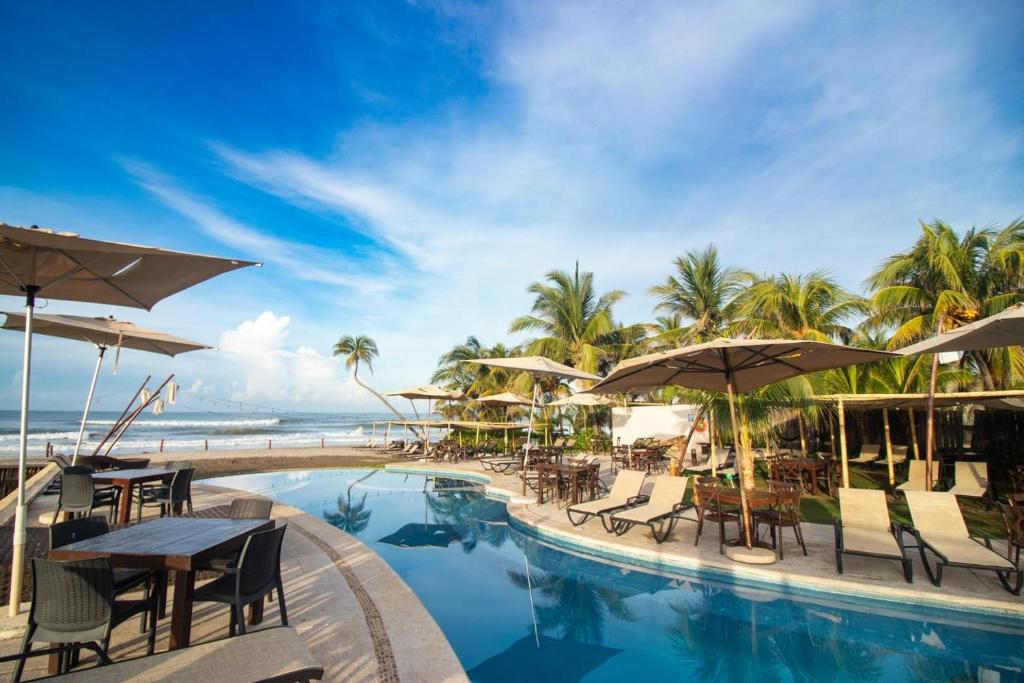 阿卡普尔科Mishol Bodas Hotel & Beach Club Privado的一个带桌子和遮阳伞的度假泳池和大海