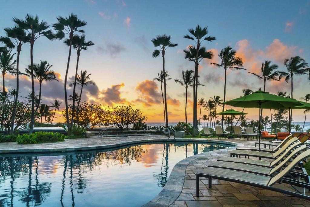 卡帕阿考艾岛怀卢阿湾希尔顿花园酒店，HI的日落时分带椅子和棕榈树的游泳池