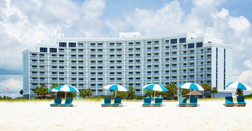 奥兰治比奇The Island House Hotel a Doubletree by Hilton的海滩上的酒店,配有椅子和遮阳伞
