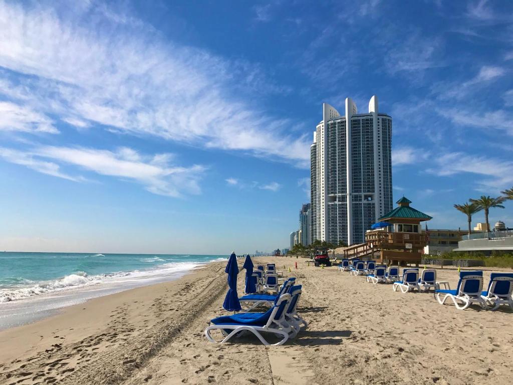 迈阿密海滩Sunny Isles Miami HOLIDAY apartment的一个带躺椅的海滩和一座高高的建筑