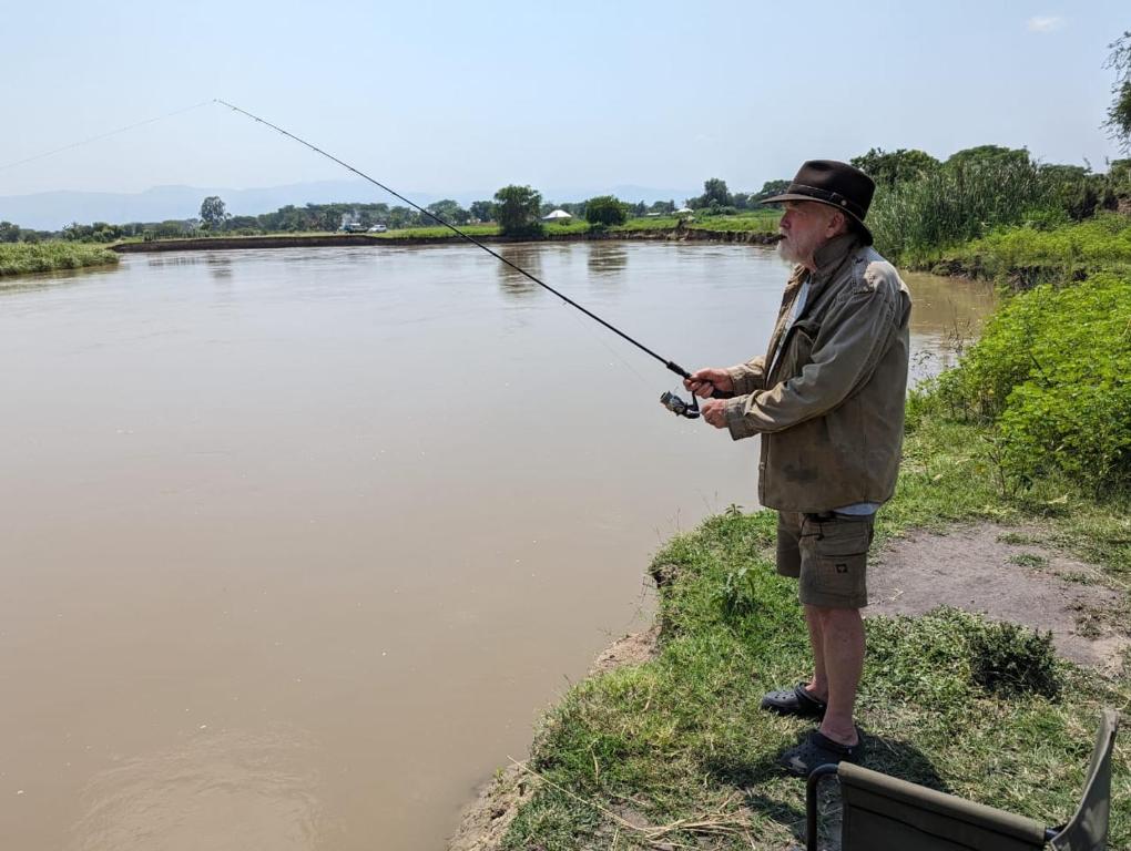 Semliki Fishing River Camp的站在河边,拿着钓 ⁇ 的人