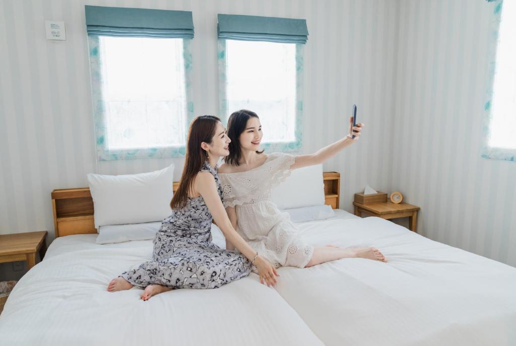 宫古岛Ecot Irabu Bridge Sunset Hills的两名妇女坐在床上,拿着一部手机