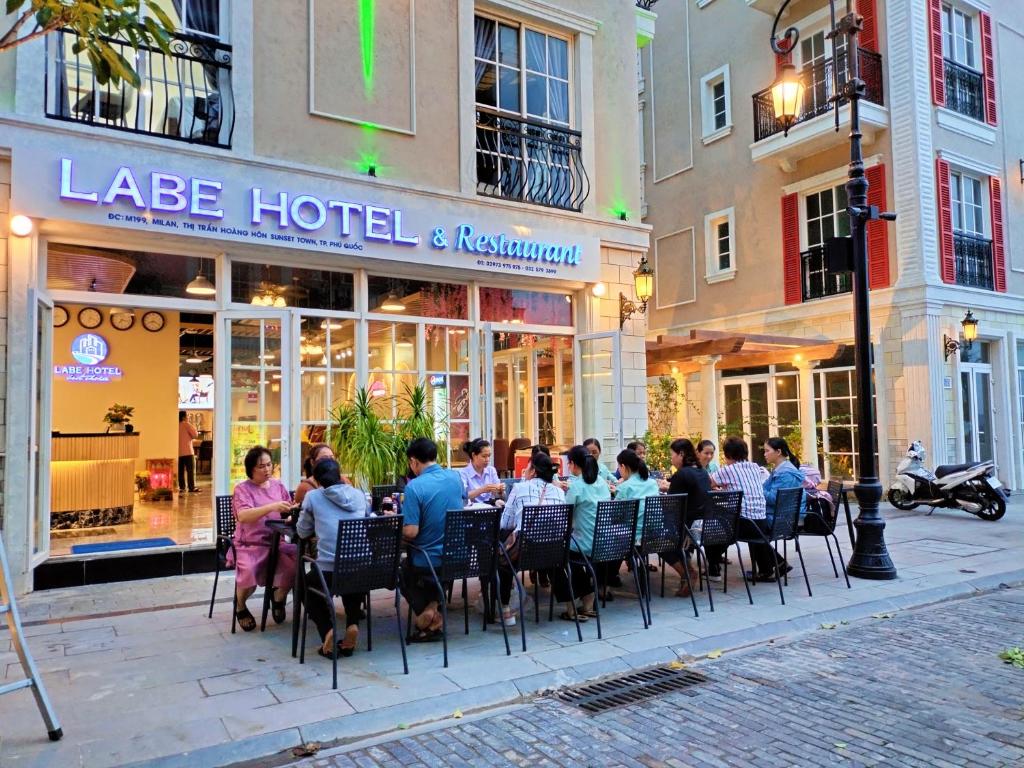 富国Labe Hotel Phú Quốc - Sunset Town - Địa Trung Hải的一群坐在酒店前桌旁的人