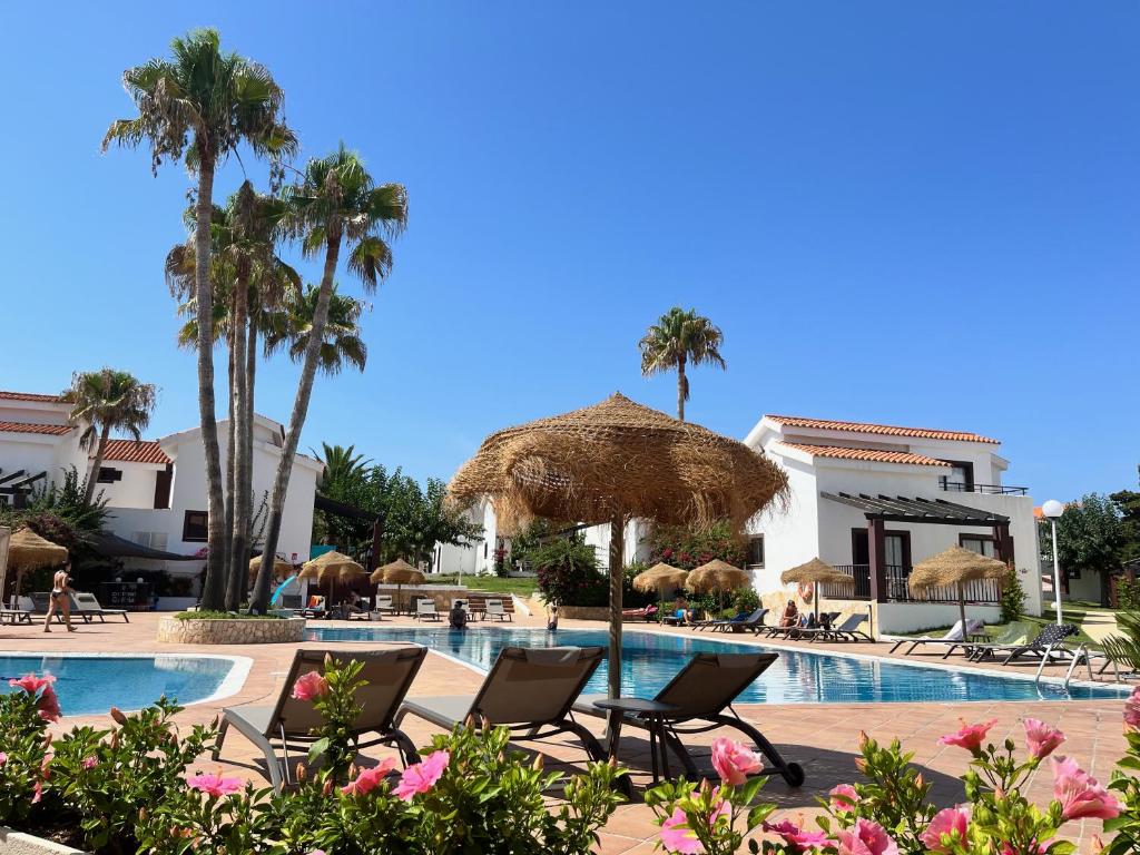 卡兰博希Nuramar Resort & Villas的一个带椅子和棕榈树的游泳池的度假酒店