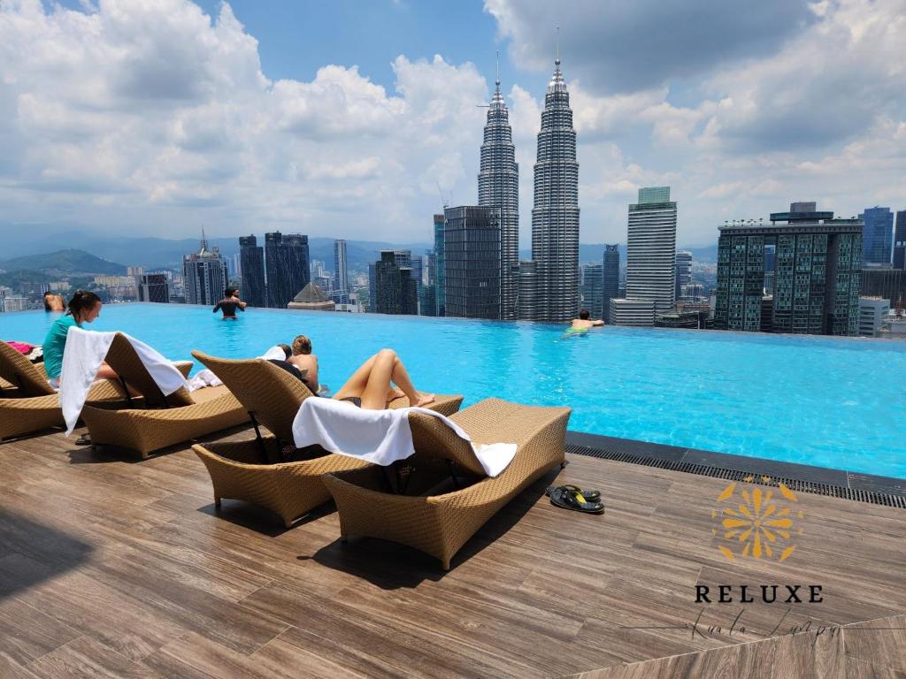 吉隆坡The Platinum 2 KLCC Premium Suite by Reluxe Kuala Lumpur的一座游泳池,里面的人坐在建筑物屋顶的椅子上
