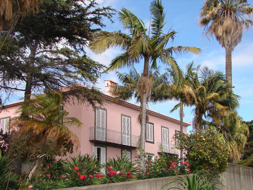 丰沙尔Quinta do Bom Sucesso的一座粉红色的房子,种植了棕榈树和鲜花