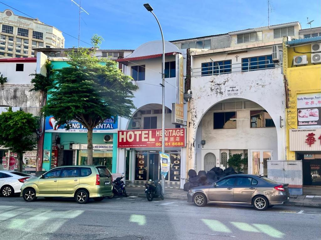 马六甲Grand Heritage Hotel的一条城市街道,汽车停在建筑前