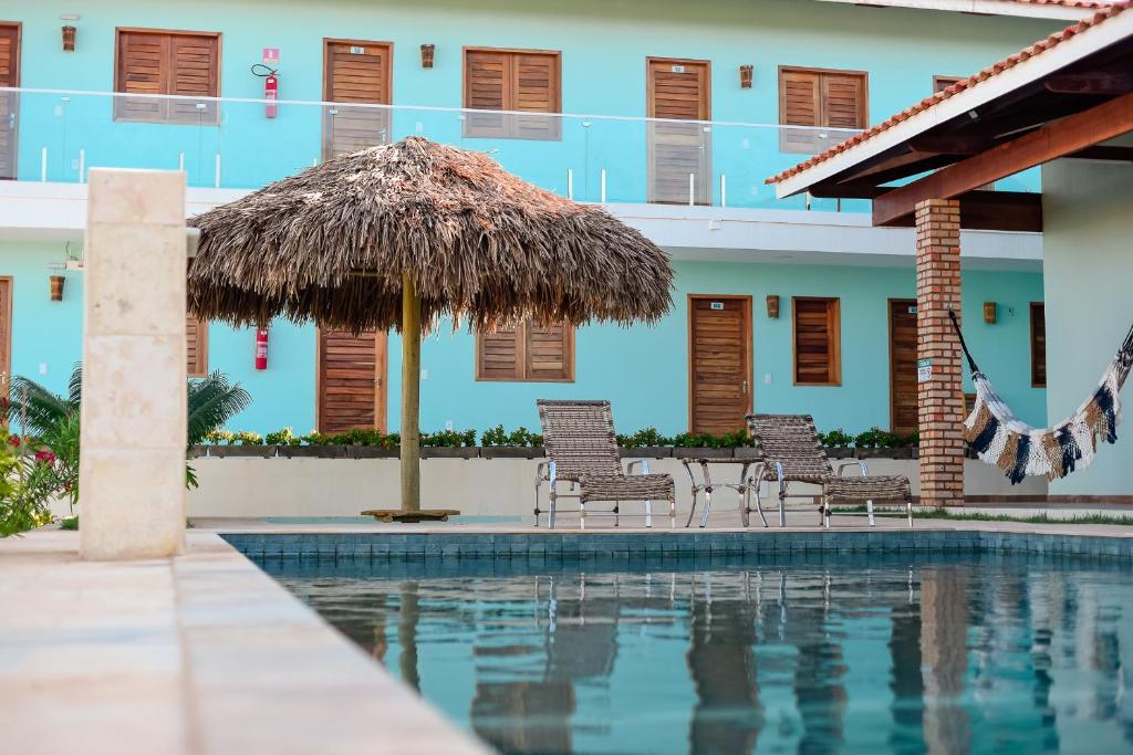 伊卡普伊Pousada Maanain的一个带椅子和草伞的游泳池的度假酒店
