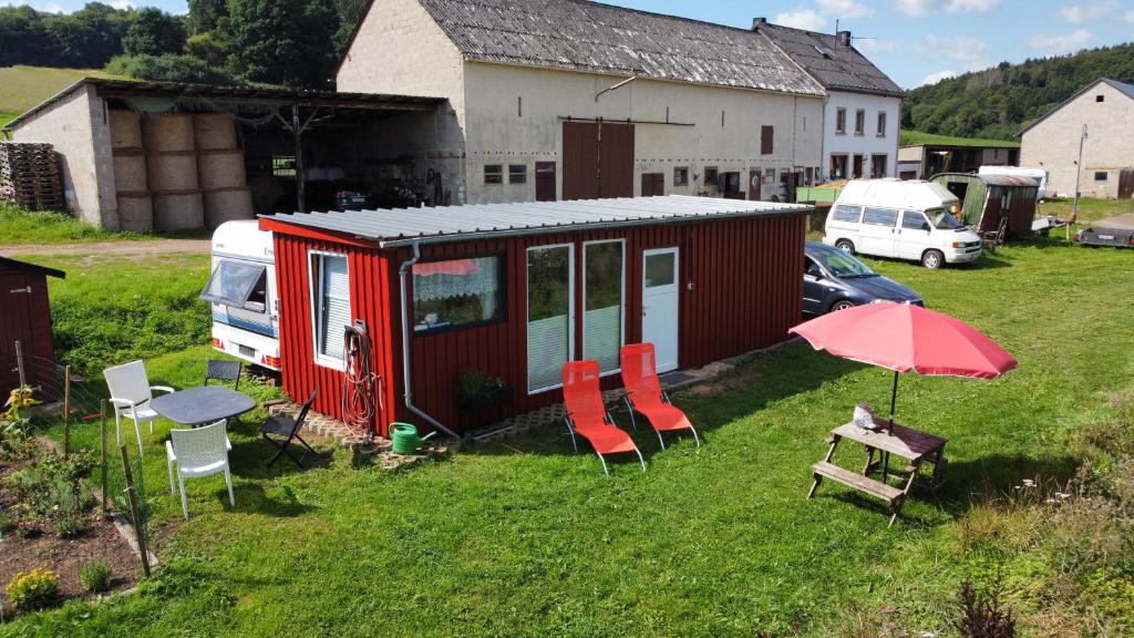 OberbettingenTiny House Anneliese Hunde okay的红色的小房子,配有椅子和桌子,还有雨伞