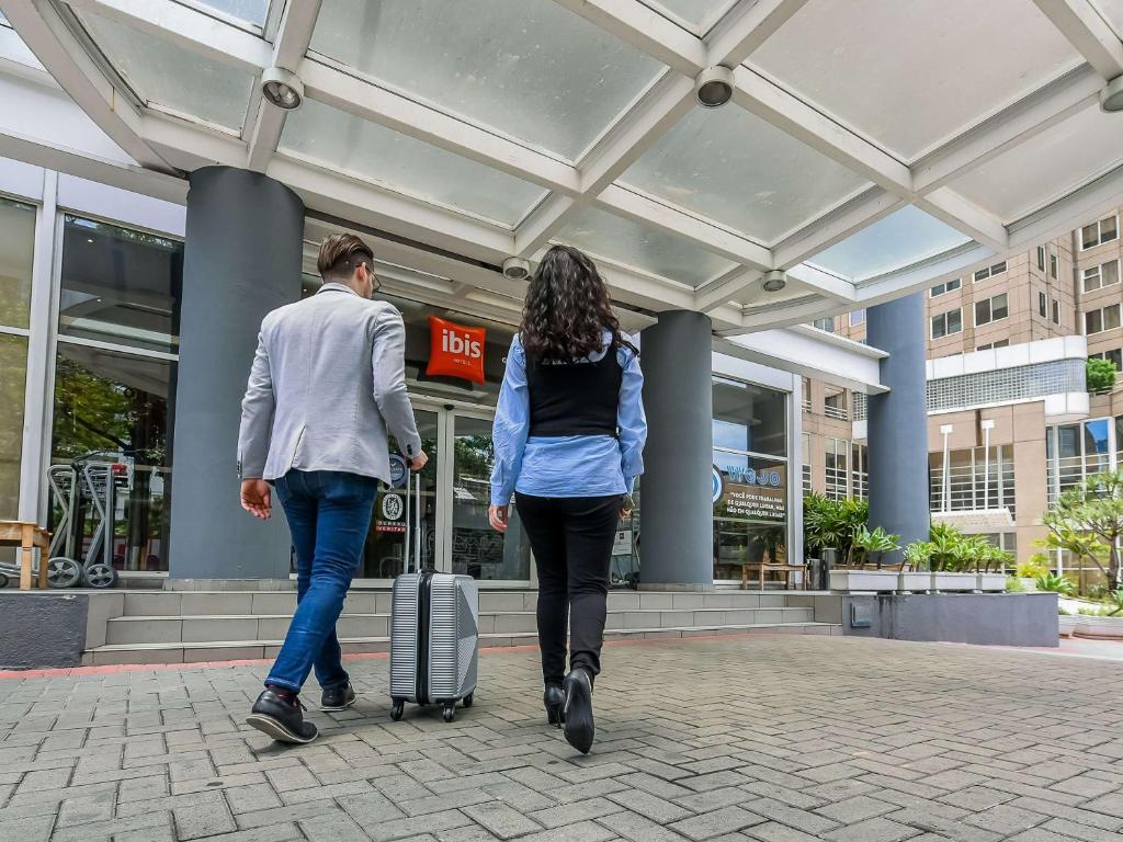 瓜鲁柳斯ibis Guarulhos Aeroporto的带着手提箱走在街上的男人和女人