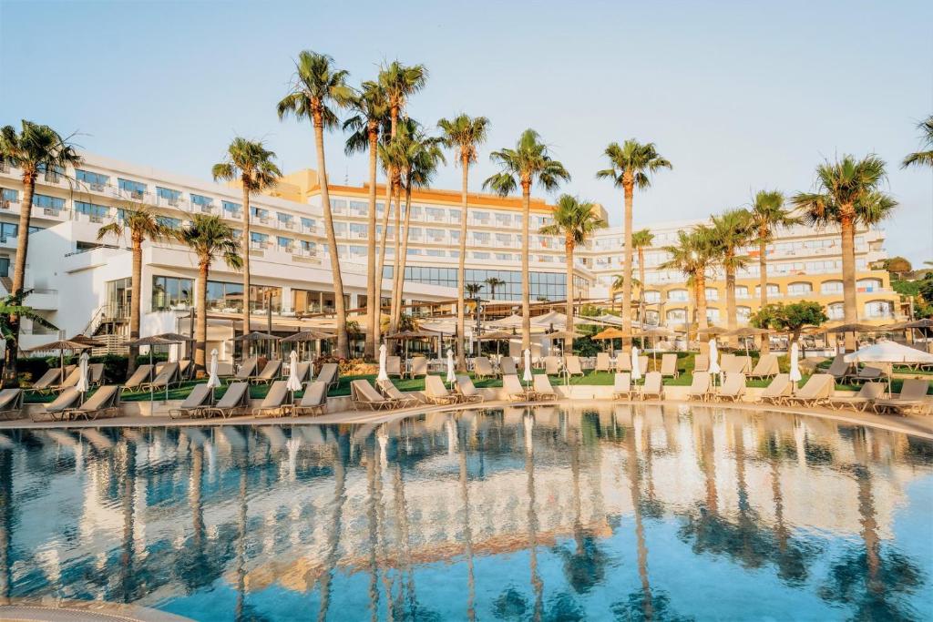 帕福斯St George Beach Hotel & Spa Resort的酒店设有带椅子和棕榈树的大型游泳池