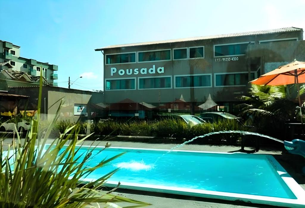 蒙加瓜Pousada Praia Mongaguá em Frente ao Mar com Piscina e Churrasqueira的大楼前带遮阳伞的游泳池