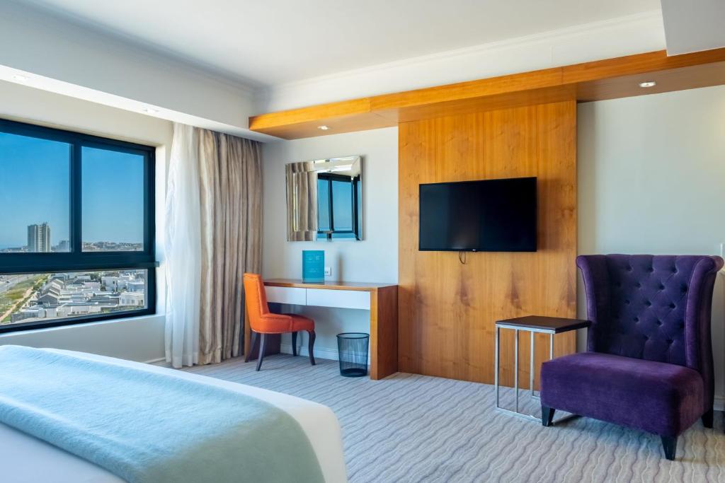 布鲁堡史特兰Blaauwberg Beach Hotel的酒店客房设有一张床、一张书桌和一台电视机。