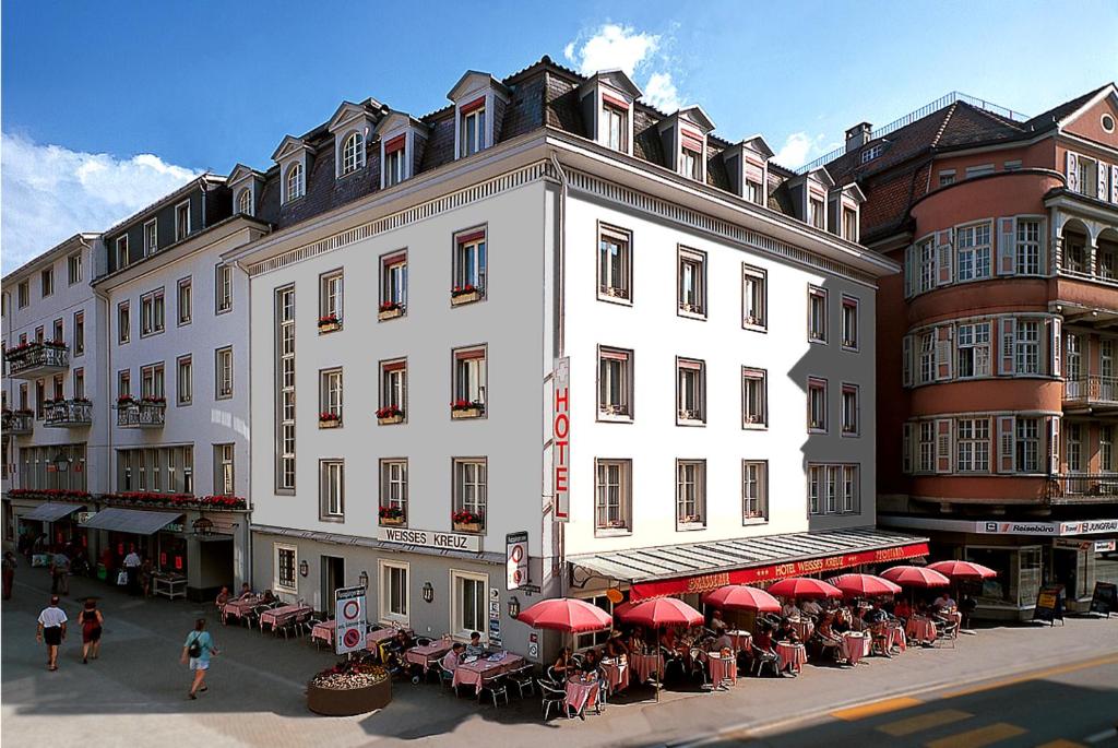 因特拉肯维赛斯克鲁兹酒店的一座带桌子和红色遮阳伞的大型白色建筑