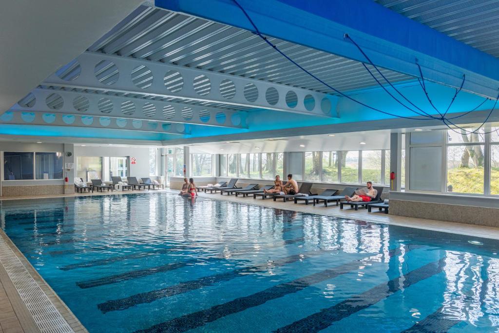 罗奇代尔曼彻斯特诺顿格兰治Spa美居酒店的一座游泳池,里面的人坐在大楼的长椅上