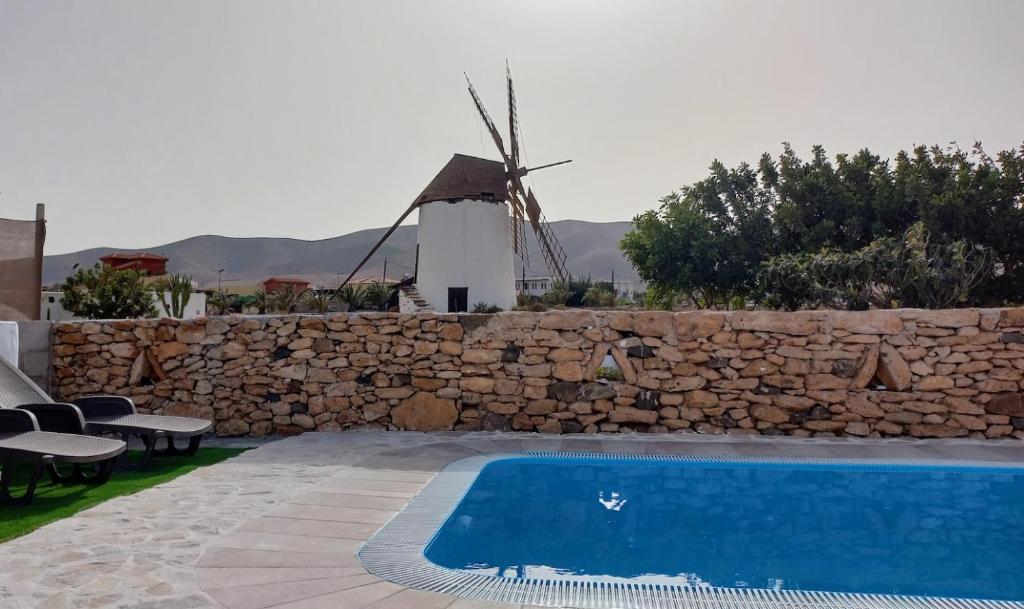 安提瓜Casita rural Molino de La Corte的一座游泳池,旁边是一座带风车的石墙