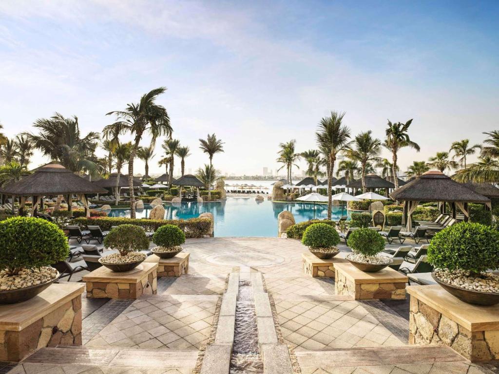 迪拜索菲特迪拜棕榈公寓酒店的一个带游泳池、椅子和棕榈树的度假村