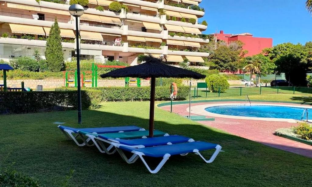马贝拉Apartamento en Marbella junto a campos de golf的游泳池畔的2把躺椅和遮阳伞