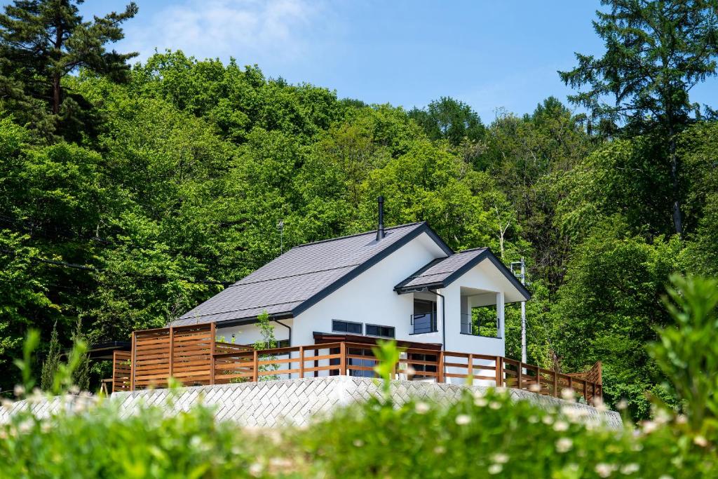 安昙野市北アルプス山麓の貸切サウナと貸別荘Azumino36stay的白色的房子,设有黑色的屋顶和木甲板