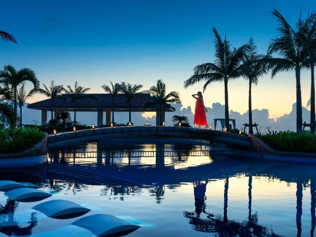 名户Oriental Hotel Okinawa Resort & Spa的穿红色衣服的女人穿过游泳池上的一座桥