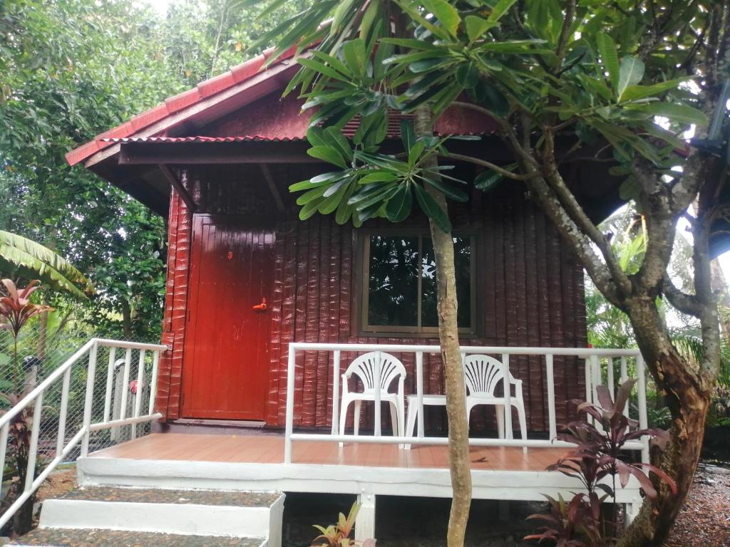北碧Thai Garden​ Resort​ Kanchanaburi​的一间红色的小房子,前面有两把白色椅子