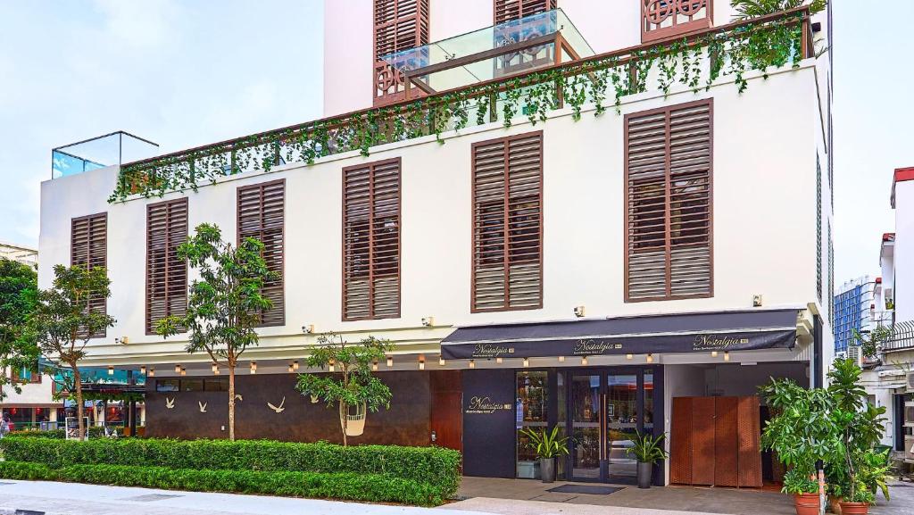 新加坡Nostalgia Hotel的白色的建筑,有棕色百叶窗和植物