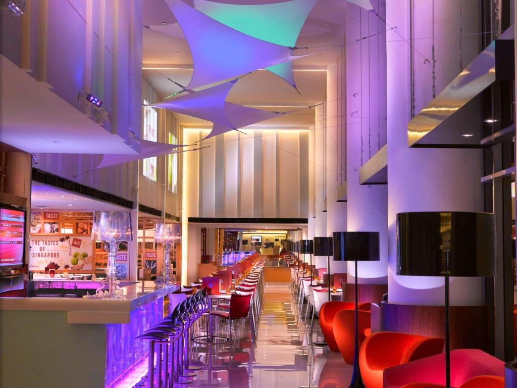 新加坡Ibis Singapore on Bencoolen的餐厅设有酒吧,配有红色椅子和紫色照明