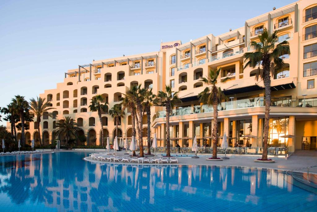 圣朱利安斯马耳他希尔顿酒店的一座棕榈树大建筑和游泳池