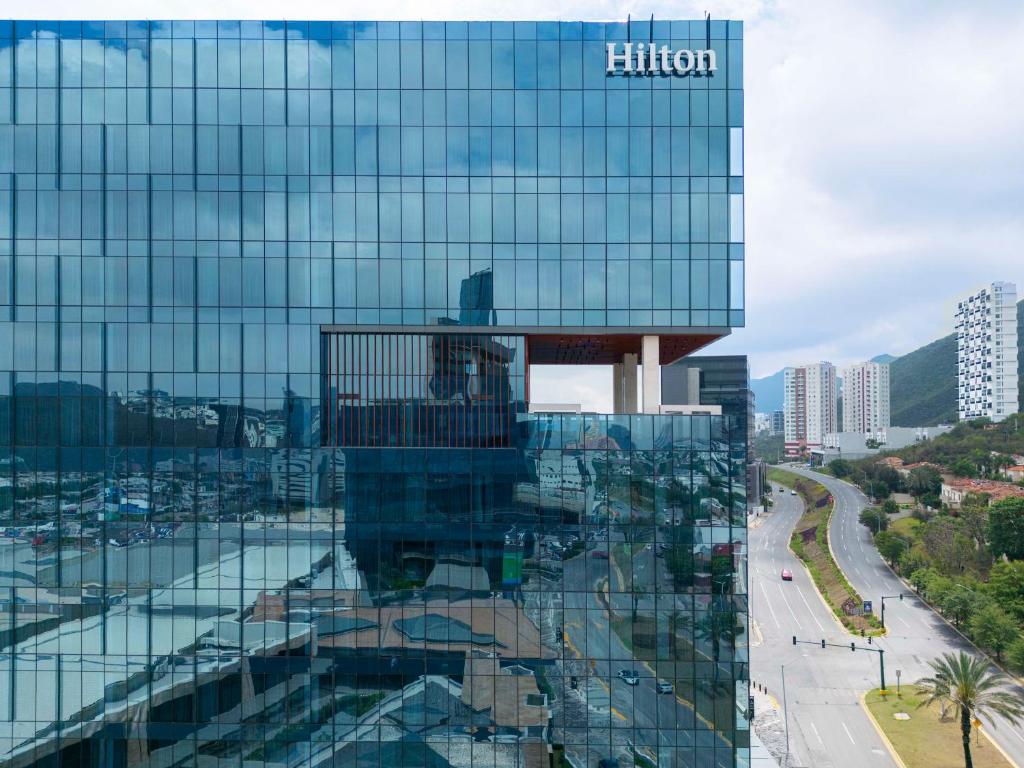 蒙特雷Hilton Monterrey的一座高大的玻璃建筑,上面有黑尔顿标志